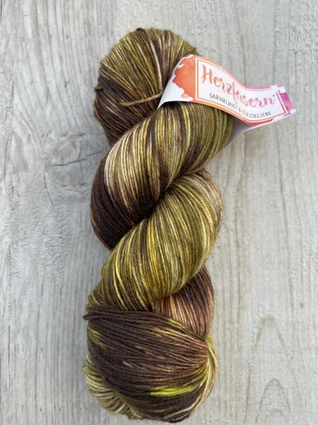 Alternativtext Bild: Strang handgefärbte Wolle in Brauntönen mit grünen Akzenten, Herzfasern No. 20 – Waldkaramell. 	•	Kontraste im Shop: Bitte Produktfoto mit heller Hintergrundfarbe belassen (Holz ist perfekt, gute Abgrenzung). 	•	Schriftgröße: Mindeste